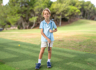 Cute little boy playing golf at the golf course in a sunny day.