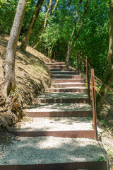 Iron steps covered with gravel rise steeply up the hillside. There is forest and green grass all around. Khuluti fortress. Georgia