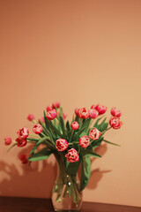 A spring bouquet of lush pink tulips in a glass vase on a beige background.