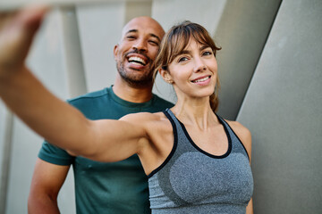 Young couple taking a selfie while posing against a wall after workout in athletic wear at urban location