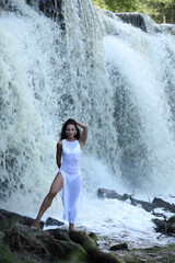 Woman in white dress posing under tropical waterfall