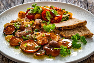 Fried saffron milk cap mushrooms with fresh salad and bread on wooden table	