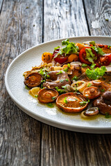Fried saffron milk cap mushrooms with fresh salad and bread on wooden table	