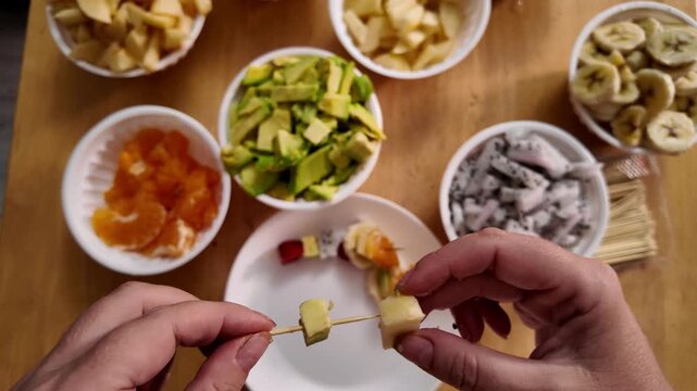 Close-up of stringing pieces of fresh fruit on a wooden skewer to make a light snack