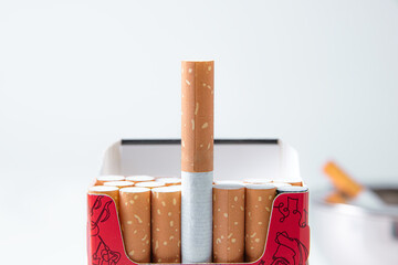 Cigarette sticking out of a cigarette box on a light background.
