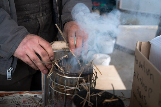 Close-up of a beekeeper preparing a smoker with straw at Dancing Bee Farm in Port Hope, Ontario, Canada, capturing the process of natural hive management and sustainable beekeeping