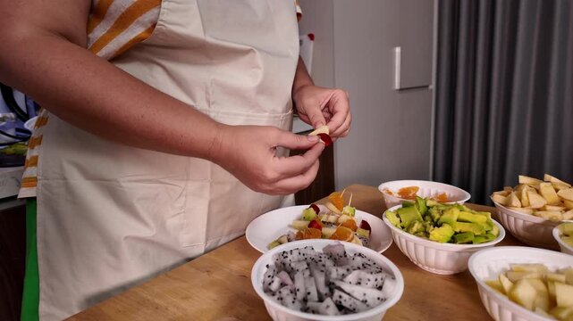 Woman makes fruit kebabs, stringing pieces of fruit on a skewer