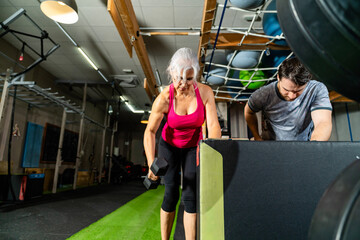 Senior woman training dumbbell rows in modern gym