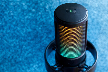 Professional condenser microphone with RGB light on blue sparkling background, concept of festive podcast or live streaming. Photo