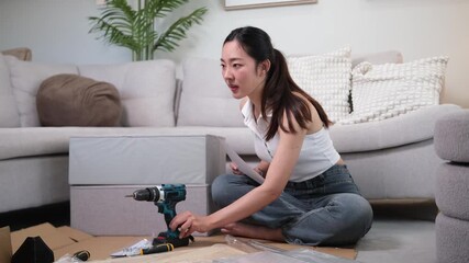 Cheerful female assembling furniture with tools, following instructions while sitting on living room floor. - Powered by Adobe