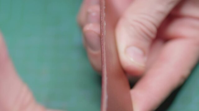 A leather craftsman makes a belt, the craftsman applies slicker to the edge of the belt blank, wipes off the remaining product with his finger and places the blank on the table.