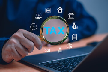 Close-up of businessman holding magnifying glass focusing on the word TAX with digital finance icons. Concept of tax investigation, financial audit and online taxation analysis