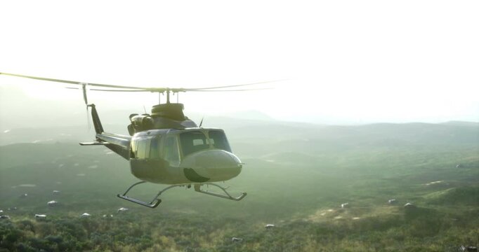 A helicopter flies effortlessly above vibrant green mountains, basking in the warm hues of sunset. The landscape stretches endlessly, dotted with patches of trees and valleys.