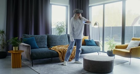 Elderly woman in virtual reality headset playing video game at home - Powered by Adobe