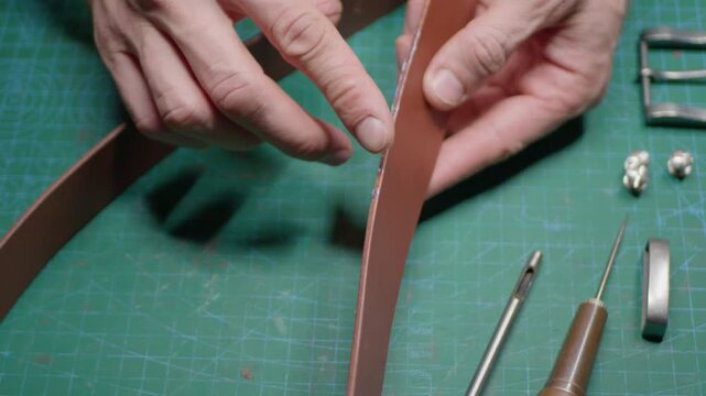 A leather craftsman makes a belt by applying edge treatment to the leather with his finger, then rubbing it with a slicker