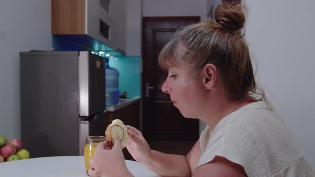 A woman eats a fresh pie with an appetite, sitting at the kitchen table