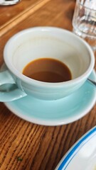 Half-empty cup of coffee in a light blue mug on a wooden table. Concept of morning routine, caffeine break, and cozy cafe atmosphere
