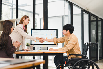 Young professional woman shaking hands with colleague wheelchair modern office desk during successful meeting, optimistic collaborative atmosphere