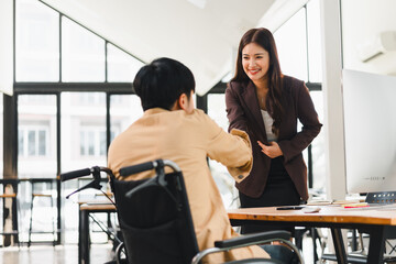 Friendly businesswoman greeting seated man in wheelchair with warm smile during office meeting