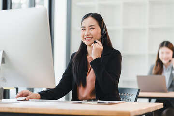 Friendly female call center agent with headset smiling while working computer modern office, confident customer service representative offering
