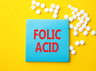 Folic acid symbol. Concept word Folic acid on blue note. Beautiful yellow background with pills. Medicine and Folic acid concept. Copy space