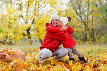 Bright autumn day features a mother and child having fun together, surrounded by vibrant yellow and orange leaves in a park