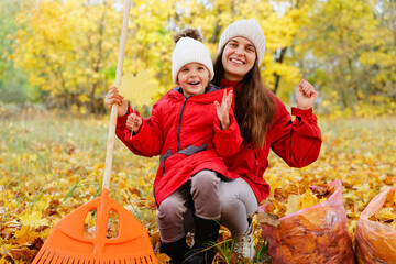 A smiling mother and her cheerful child gather leaves in a bright autumn park filled with yellow trees