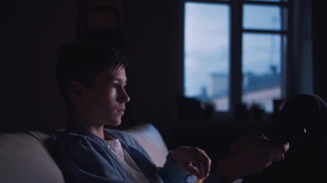 Evening Wind-Down: Young Boy Relaxing on the Couch and Changing TV Channels