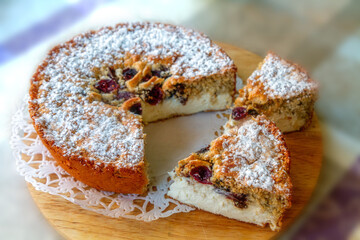 A delicious homemade pie with cottage cheese and berries, dusted with powdered sugar, served on a wooden board. This rustic dessert features a cut-out slice and a sweet pastry perfect for baking