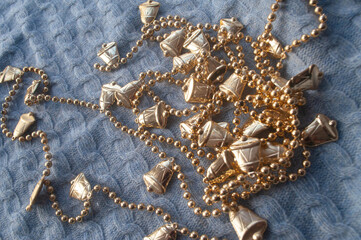 Golden Christmas tree decoration, long garland with bells and beads on a thread on blue knitted background