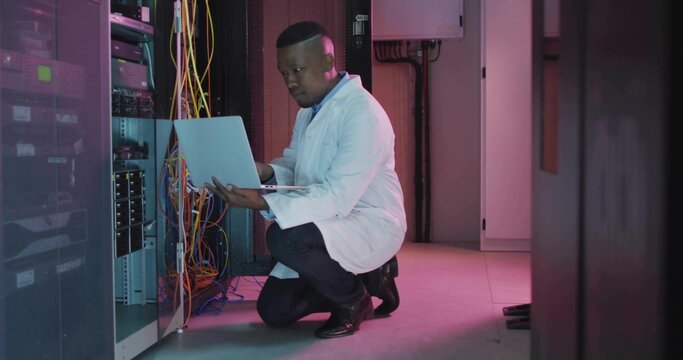 Kneeling IT technician wearing lab coat typing on laptop in server room, with Ethernet cables - Powered by Adobe
