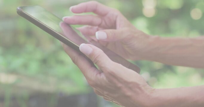 Tapping adult woman in short-sleeved top and swiping tablet computer in garden, with sunlight