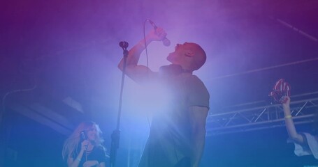 Gripping microphone singer belting out song on stage, with red maracas and colored LED lights