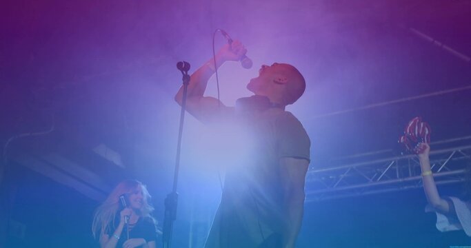 Gripping microphone singer belting out song on stage, with red maracas and colored LED lights