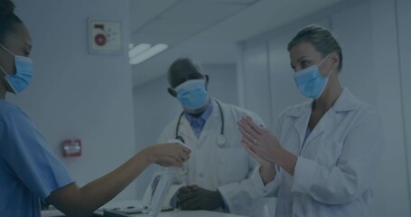 Offering masked nurse in scrubs passing disinfectant spray to masked doctor at hospital desk