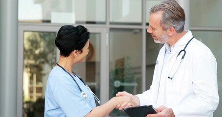 Doctor in lab coat shaking hands with scrub-clad nurse at glass doors, with stethoscopes and tablet