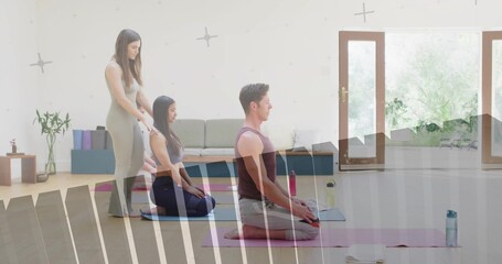 Guiding yoga participants kneeling on pink, purple mats in bright studio, with blocks and plants
