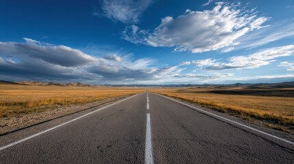 Fototapeta premium Straight open road cutting through a vast golden grassland with rolling hills under a dramatic blue sky, representing endless possibilities, movement, discovery, and the solitude of travel
