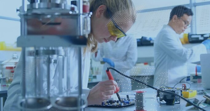 Female engineer in lab coat soldering circuit board in electronics lab, with soldering iron