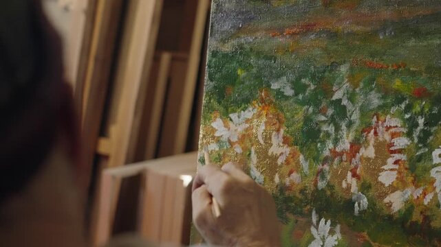 Senior artist on a wheelchair paints an oil painting on canvas in a studio