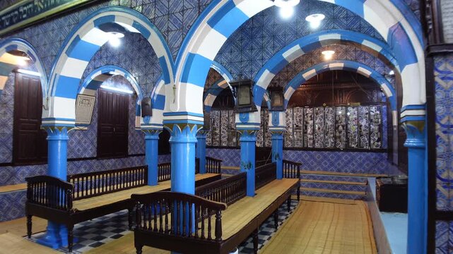 Walking towards blue white arches inside the beautiful El Ghriba synagogue on Djerba island, religion and history in Tunisia