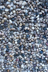 Close-up macro texture of a pebble-dash wall. A collection of small, smooth, colorful river stones and pebbles embedded in concrete for a background