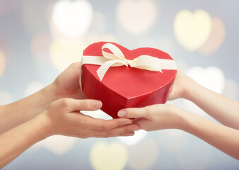 Hands exchange heart-shaped gift box in pastel blur, symbolizing affection, generosity, and the ritual of emotional giving.