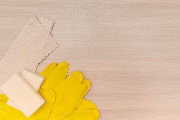 Yellow rubber gloves on wooden tabletop, microfiber cleaning cloth.