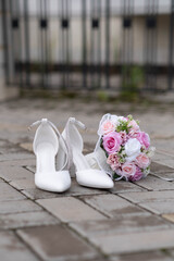 Chic white heels gracefully paired with a stunning pastel rose bouquet resting on charming cobblestone.