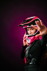 Woman wearing pink motocross gear poses confidently with helmet in a studio setting
