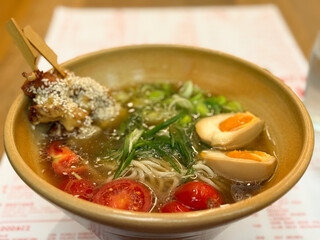A bowl of ramen with egg, cherry tomatoes and sesame chicken. Asian cuisine, comfort food and dining experience representing balance, flavor and culinary aesthetics.
