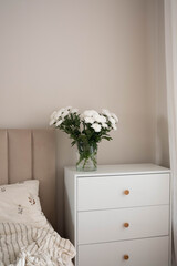 A serene bedroom with a charming nightstand and delicate white Chrysanthemum flowers, perfect for relaxation and comfort.