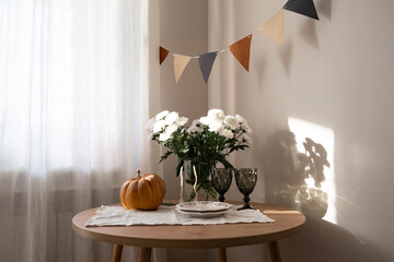 A warm and cozy autumn setting is beautifully adorned with Chrysanthemum flowers, a cheerful pumpkin, and festive bunting.