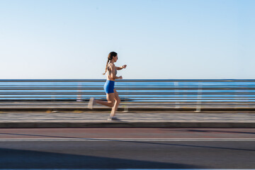 Young woman running on coastal road, staying active and focused on her fitness goals